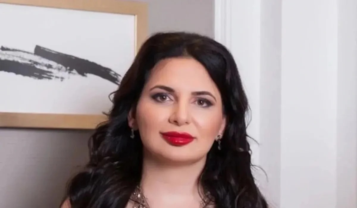 Image of Mr Ruja Ignatova, wearing lipstick and a poster in her background